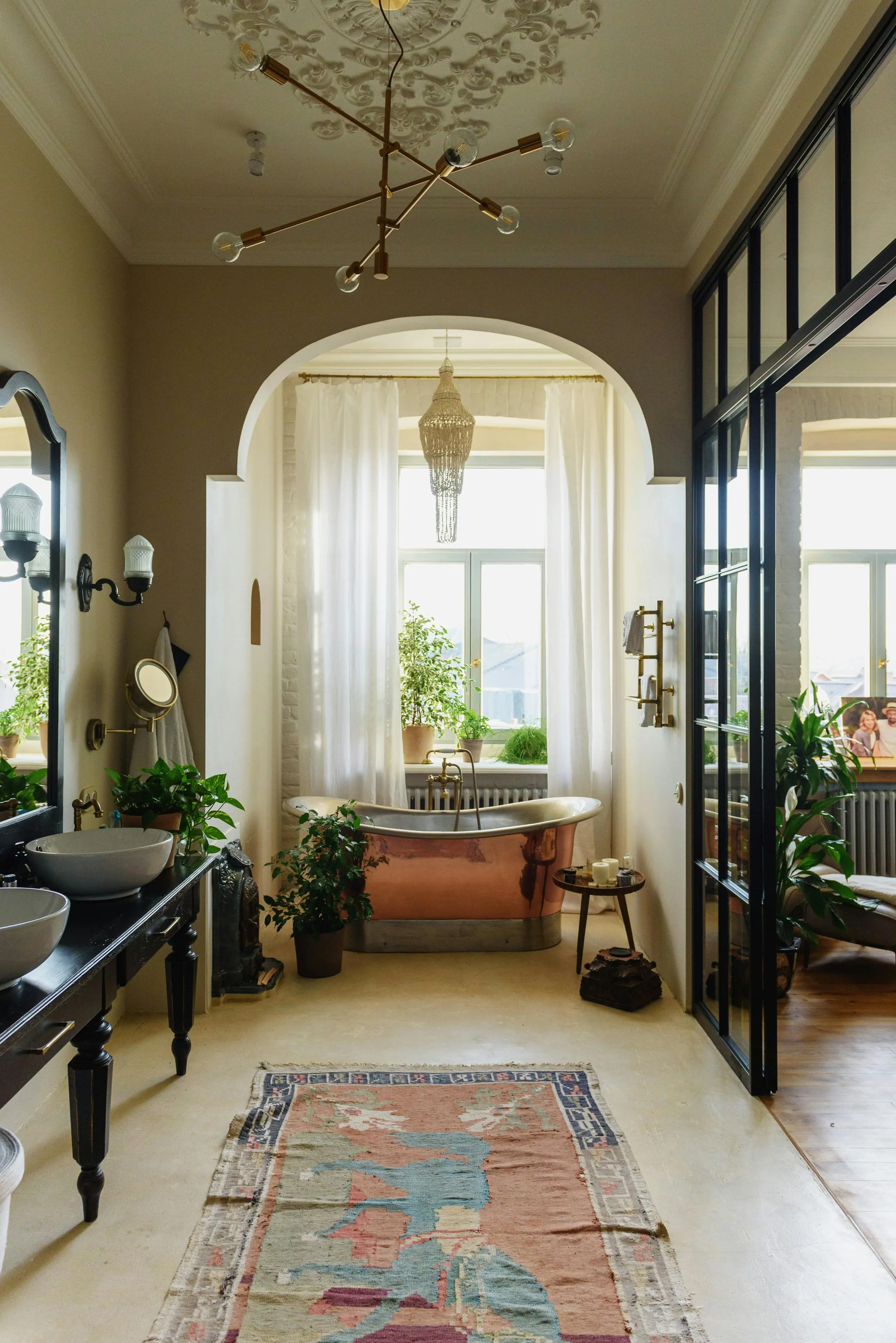 Elegant bohemian bathroom featuring copper freestanding tub in arched alcove with vintage chandelier and tropical plants