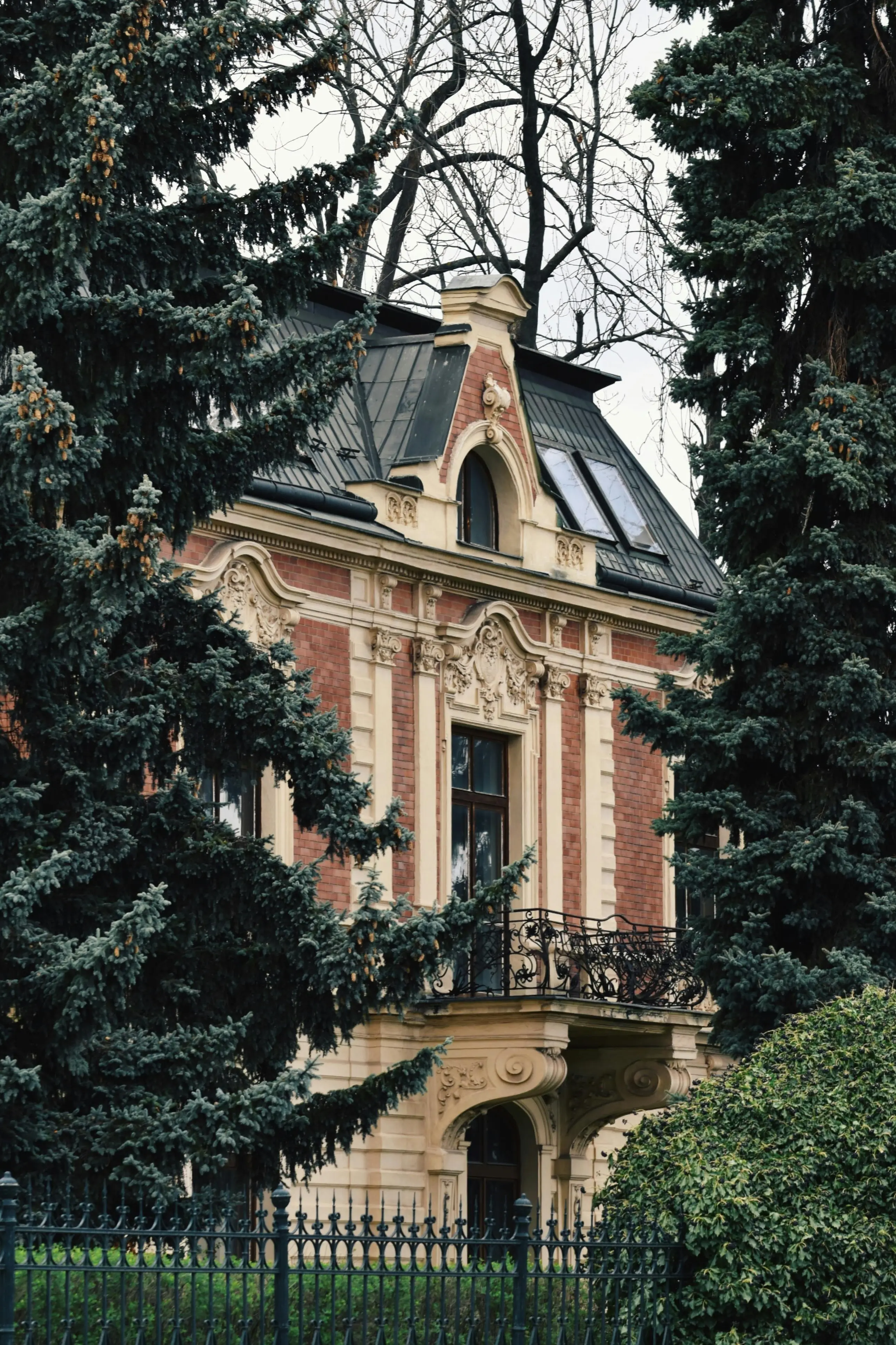 Historic European chateau with ornate baroque architecture, mansard roof, iron balcony and mature evergreen trees