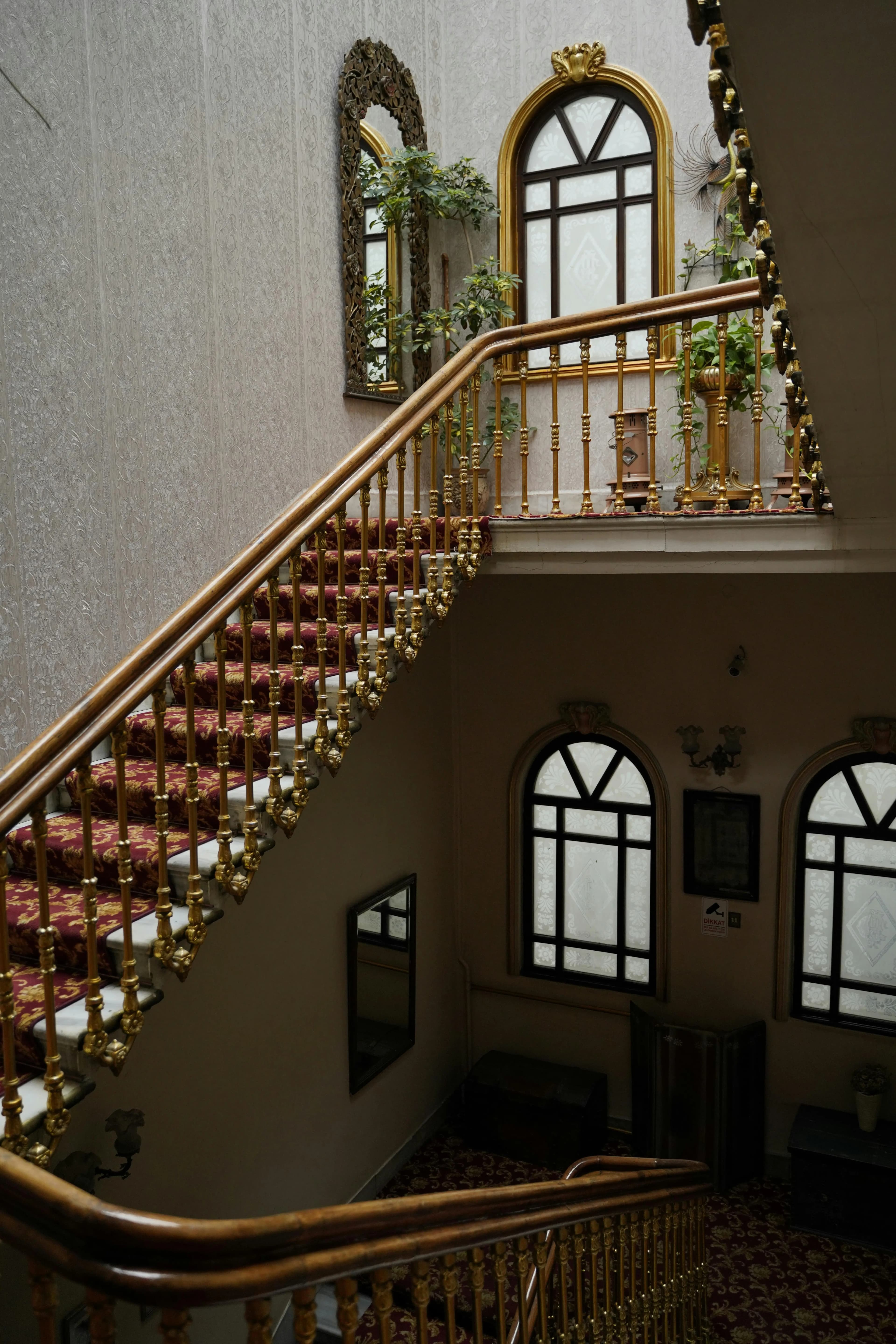 Ornate grand staircase with gold spindle railing, carpeted treads, arched windows and classical balustrade