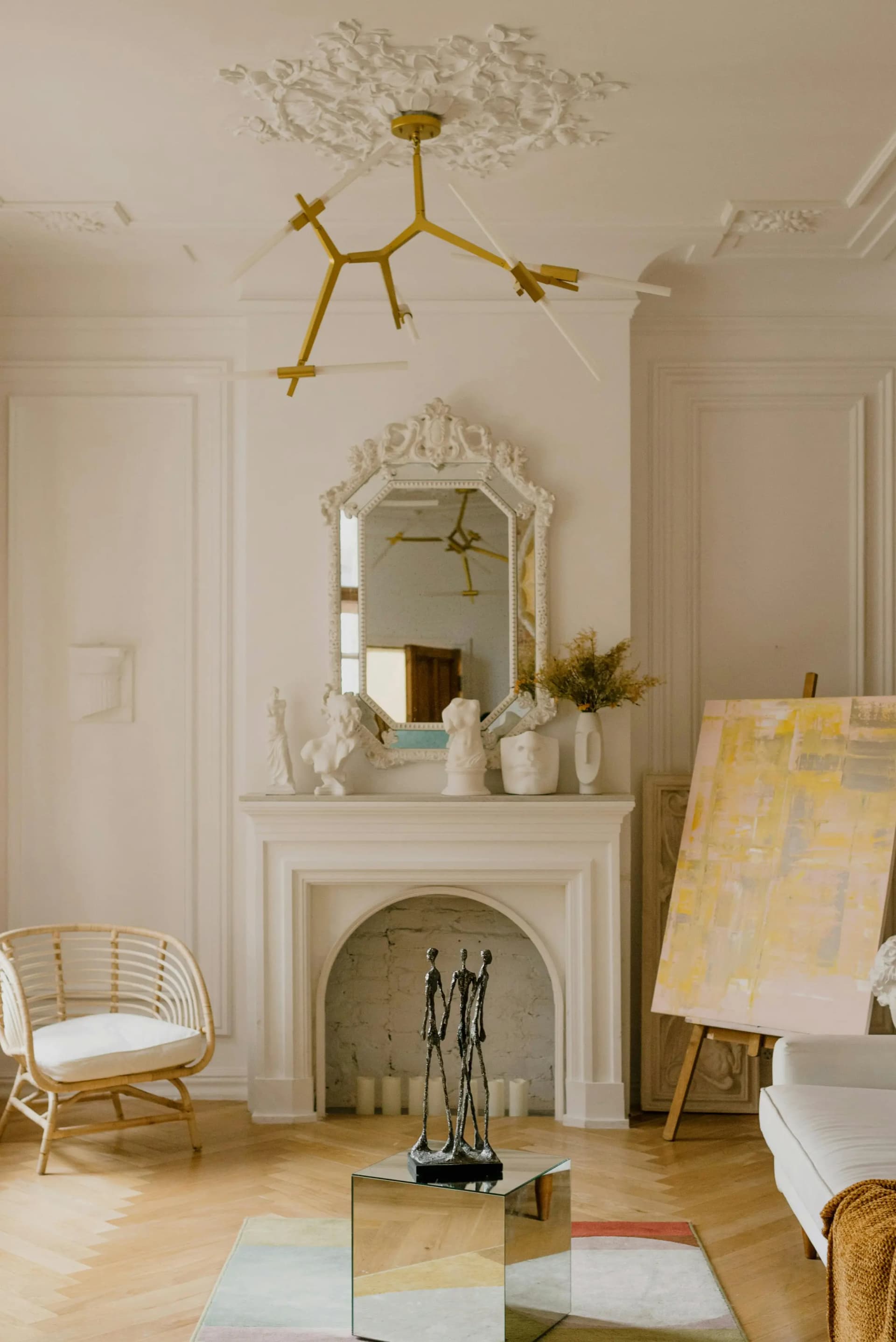 Parisian-style living room with ornate white fireplace mantel, gold sputnik chandelier, and contemporary art on easel