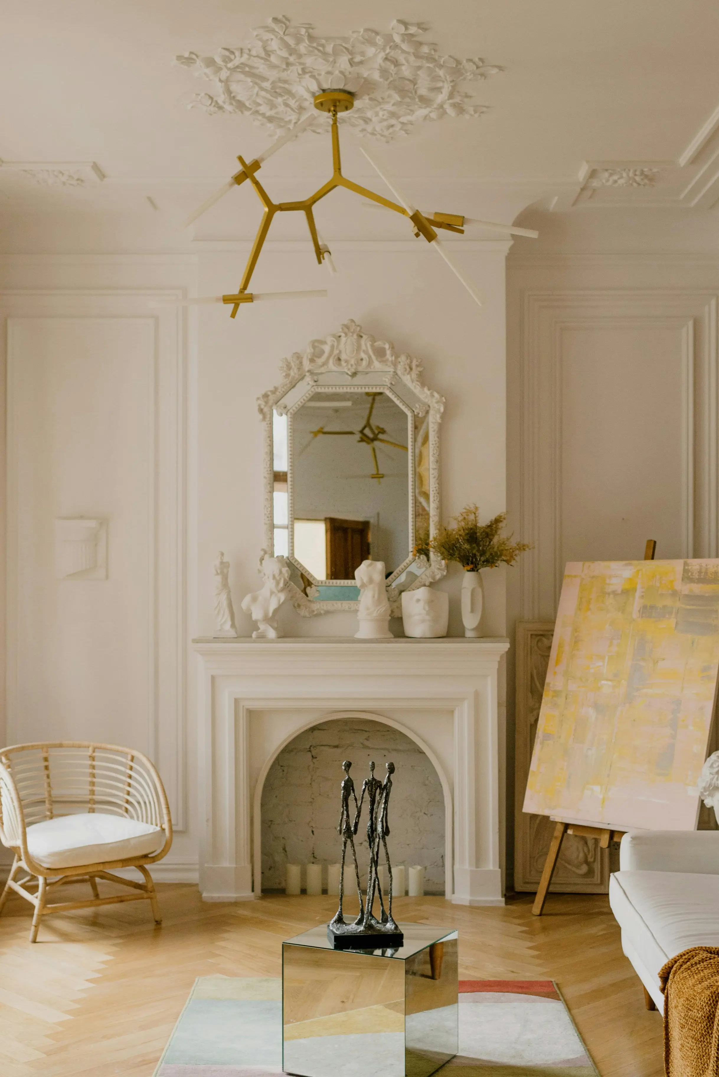 Parisian-style living room with ornate white fireplace mantel, gold sputnik chandelier, and contemporary art on easel