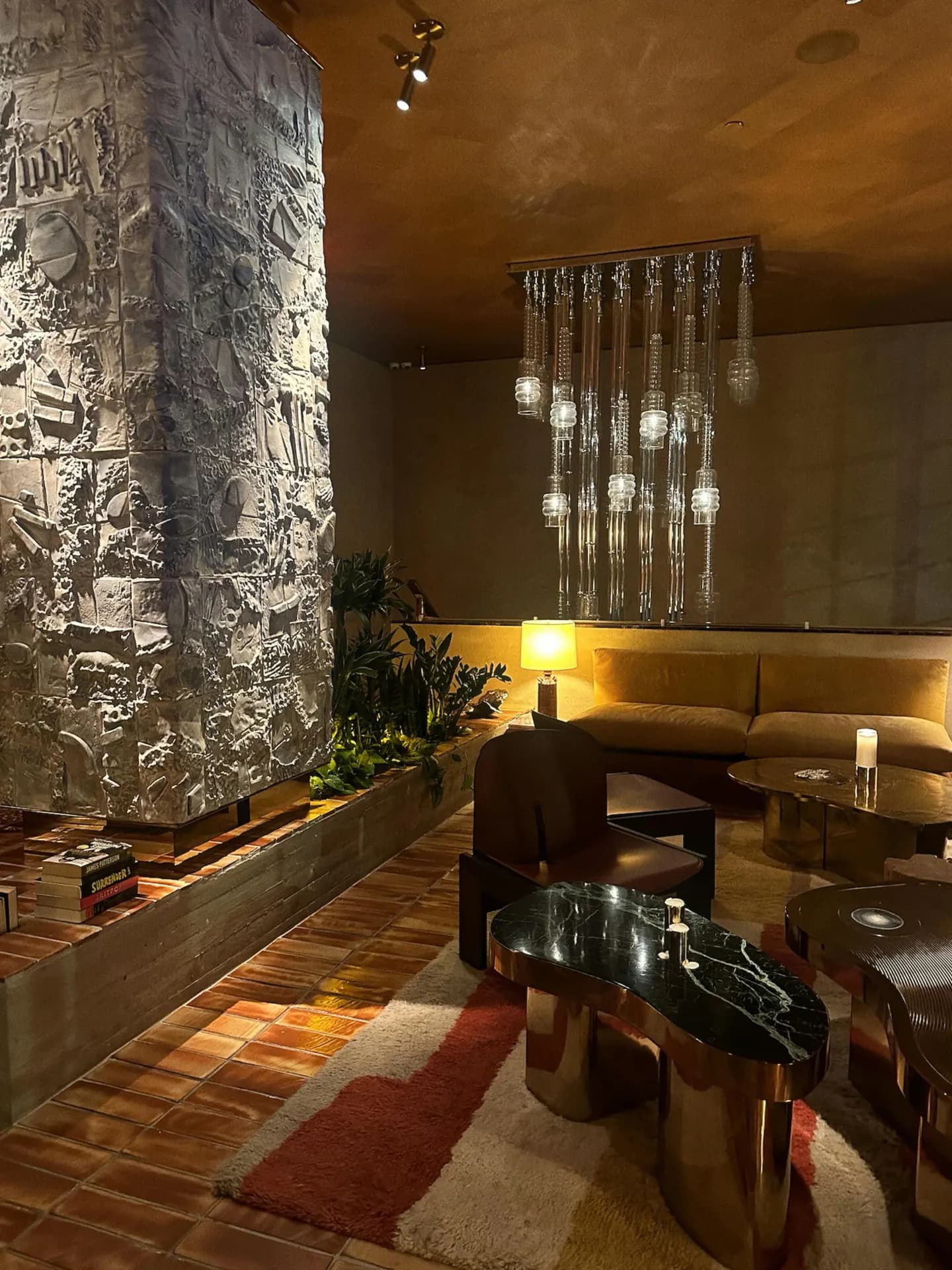 Moody designer lounge with sculptural stone fireplace column, cascading glass chandelier and velvet curved seating